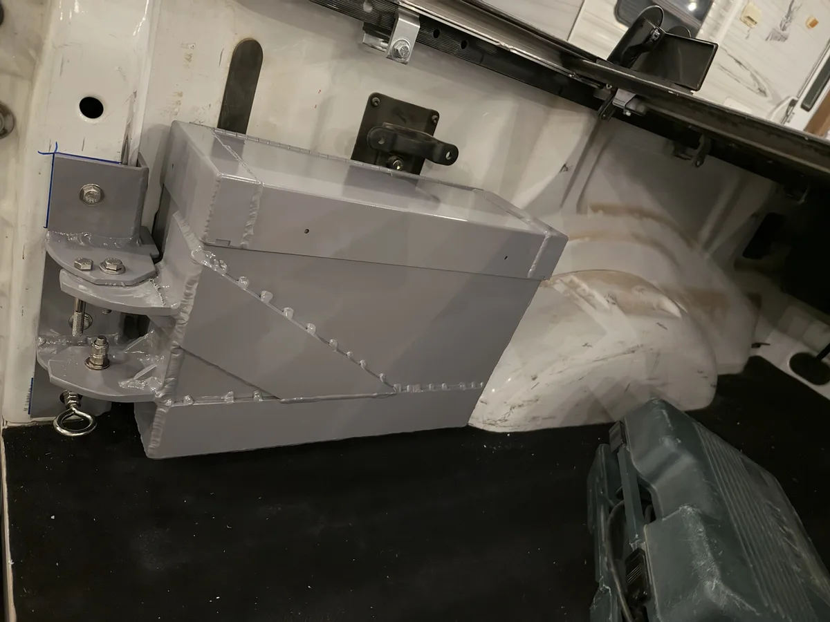 A close-up photo shows a newly installed gray metal box mounted inside a white truck bed, secured with bolts and partially…