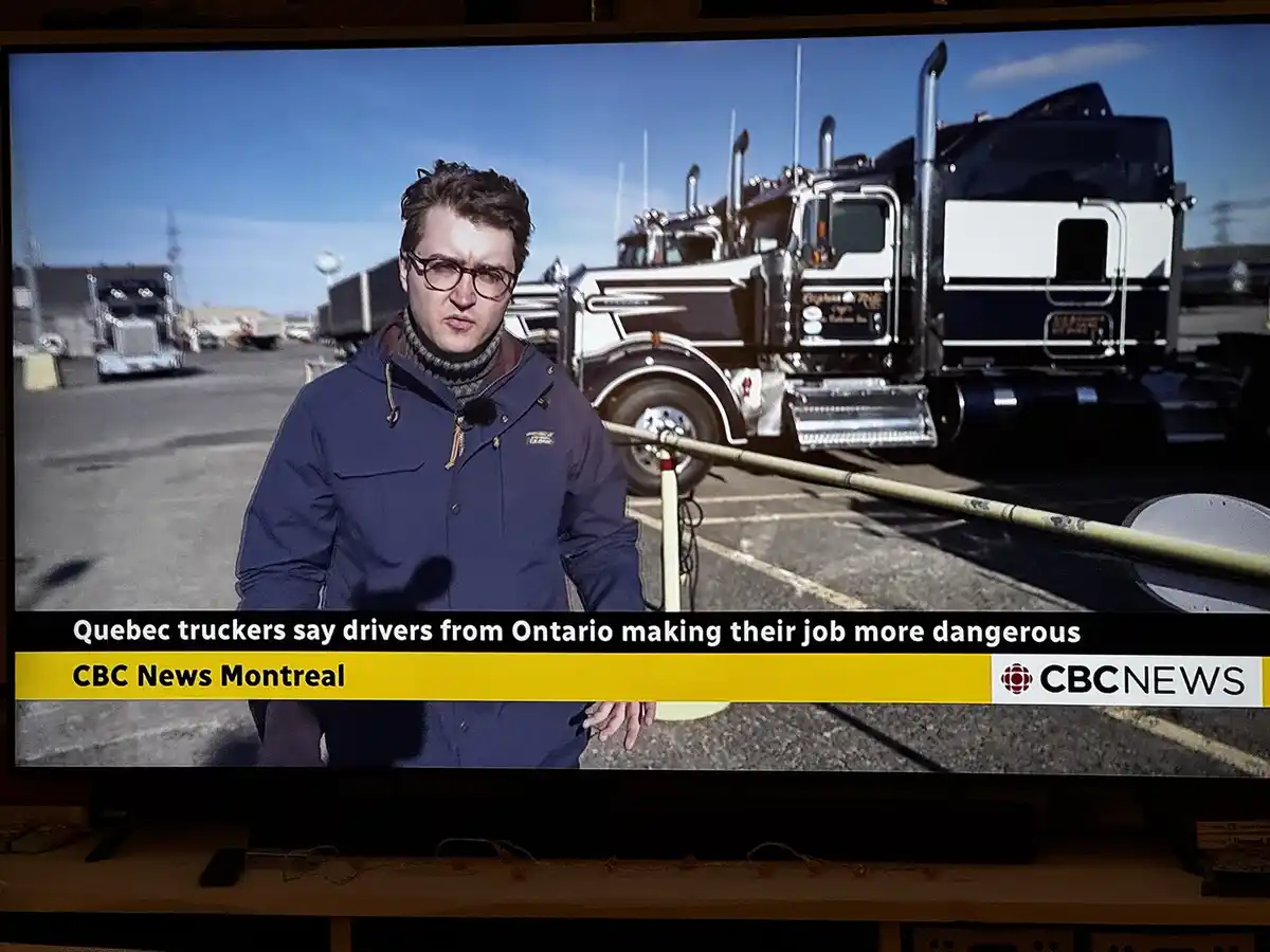 A news broadcast from CBC News Montreal shows a male reporter in a blue jacket and glasses standing in front of large…