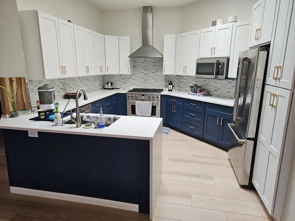 A modern kitchen with white upper cabinets, navy blue lower cabinets, and stainless steel appliances, overlaid with the text…