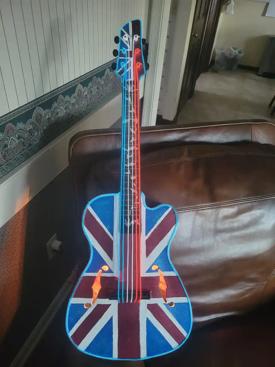 A handmade electric guitar with a Union Jack flag painted on its body and neck, outlined with glowing blue and red neon…