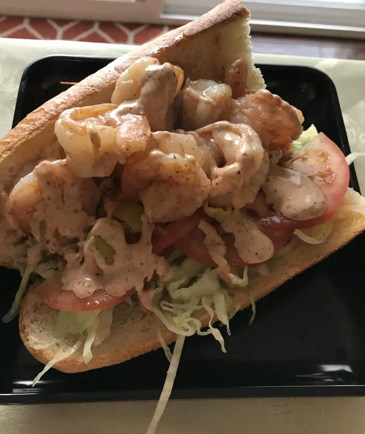 A close-up photo shows a shrimp po'boy sandwich overflowing with large cooked shrimp, a thick creamy sauce, shredded…