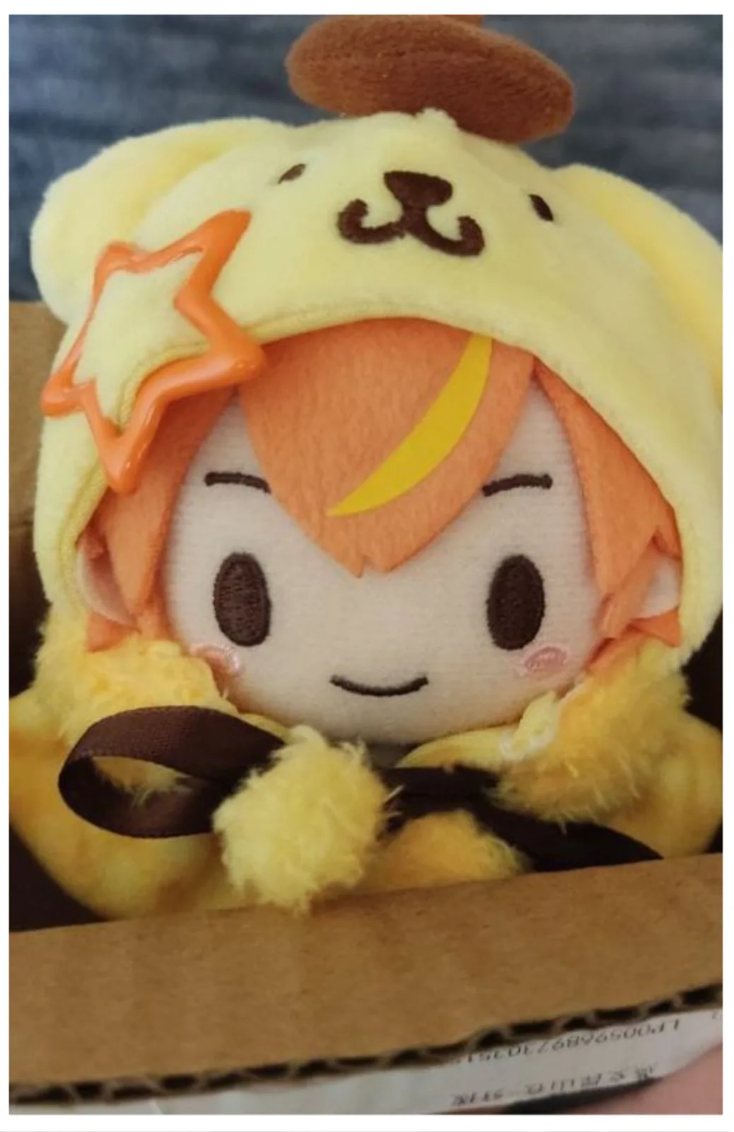 A plush toy of the anime character Kizuna AI wearing a yellow dog-themed hood with ears and a brown bow, winking with closed…
