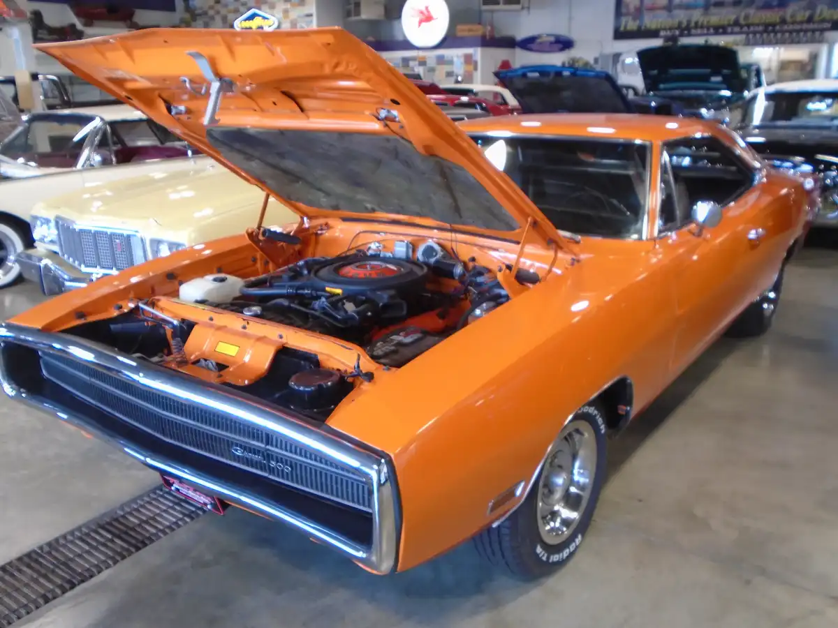 a bright orange classic dodge charger with its hood open, revealing the engine, is parked inside a car dealership or…