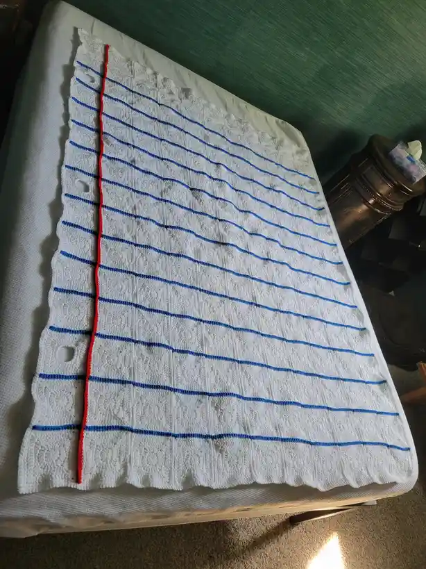 A white crocheted blanket with blue horizontal stripes and a red vertical stripe lies on a bed. The text overlay reads 'i…