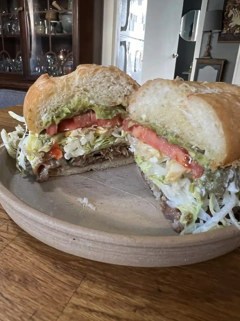 A large, generously filled sandwich cut in half and presented on a rustic ceramic plate, revealing layers of shredded…
