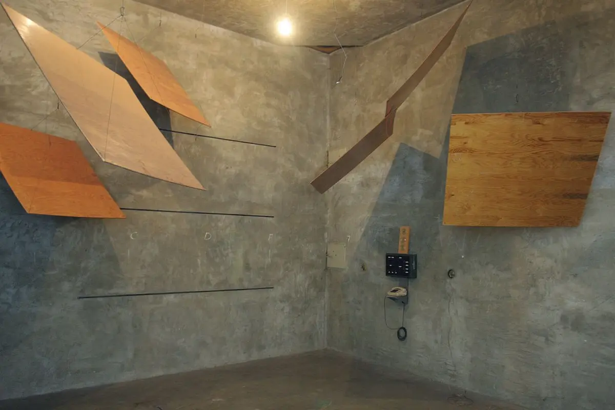 A concrete room with plywood panels suspended from the ceiling and mounted on walls, with letters C, D, F marked on one wall…