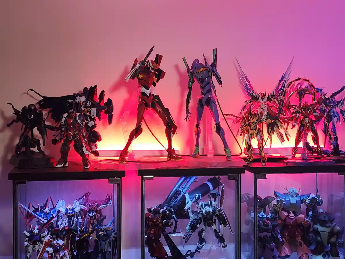 A collection of anime mecha model figures displayed on shelves under pink and orange ambient lighting. The top shelf…