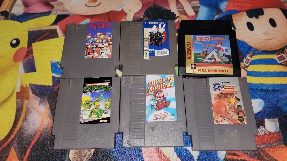 Six Nintendo Entertainment System game cartridges are arranged in two rows on a colorful rug featuring cartoon characters…