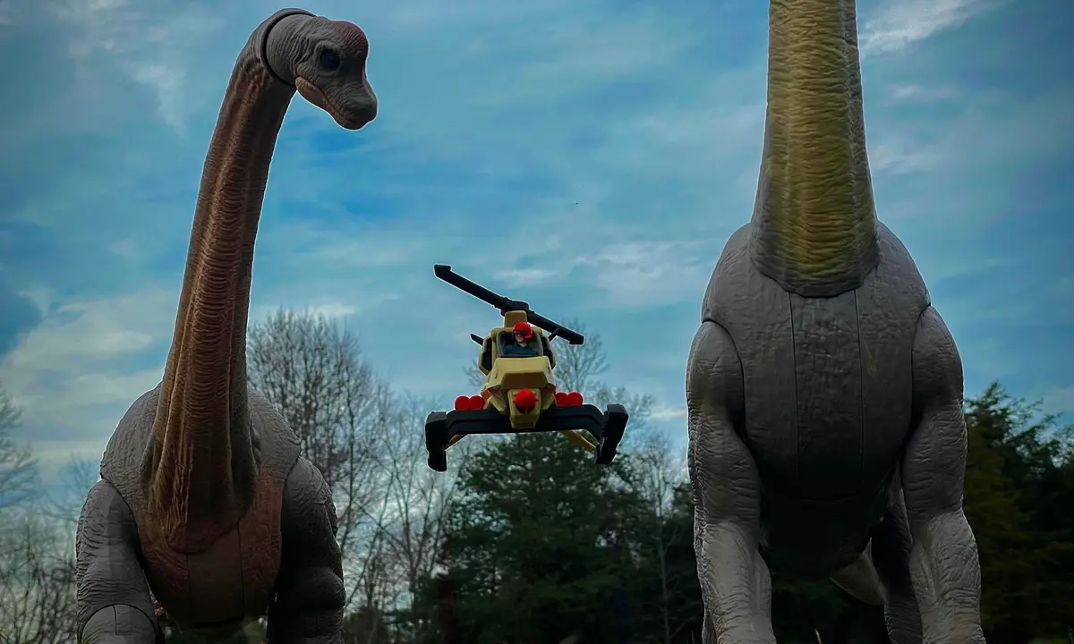 Two large, realistic-looking dinosaur statues stand on either side of the frame, facing each other with their long necks…