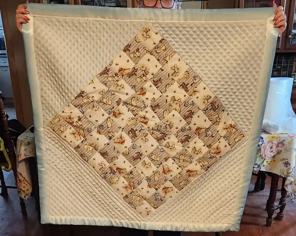 A person holds up a handmade quilt featuring a diamond-shaped pattern of Winnie the Pooh characters on a light background…