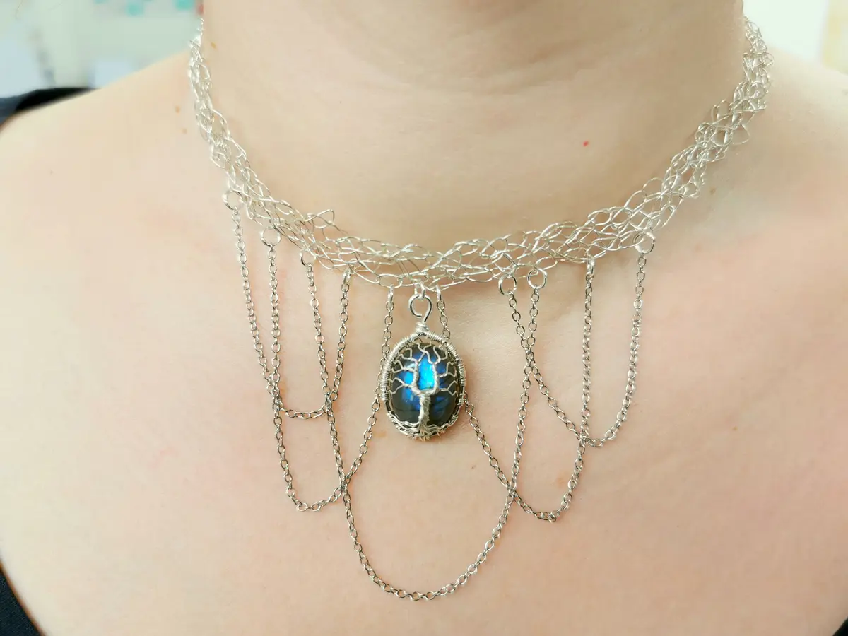 A close-up photo shows a person wearing an ornate silver necklace with a central pendant featuring a tree-of-life design…