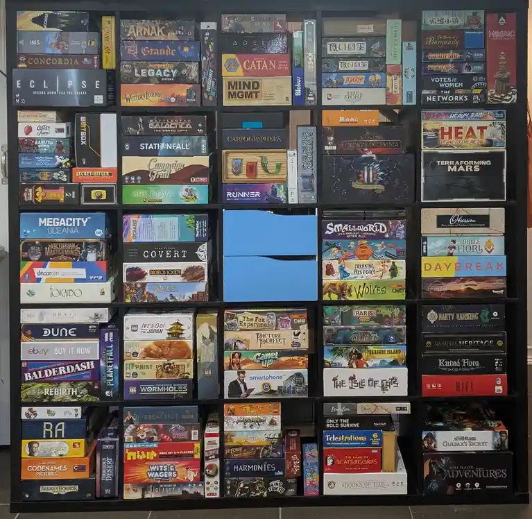 A large black shelving unit is densely packed with hundreds of colorful board game boxes, neatly arranged in rows and…