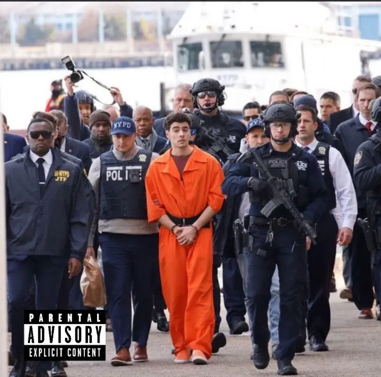 A man in an orange prison jumpsuit is being escorted by numerous police officers, some in tactical gear and others in…