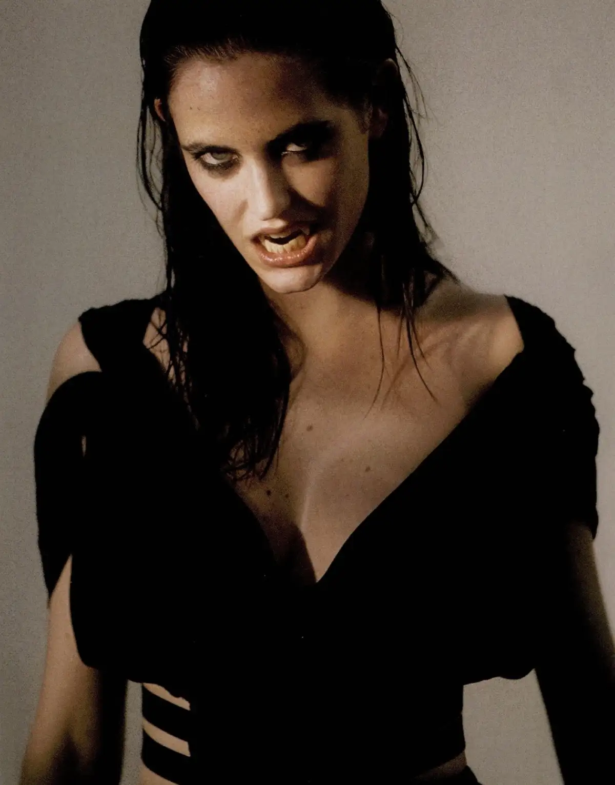 A woman with dark hair and a black top is shown with her mouth open, revealing sharp teeth and a menacing expression. The…