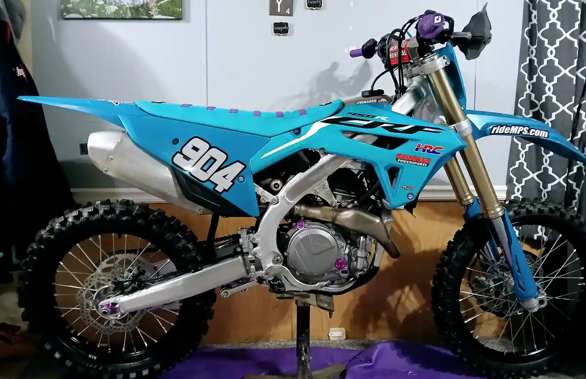 A bright blue and silver motocross bike with the number 904 prominently displayed on its side panel is parked indoors on a…