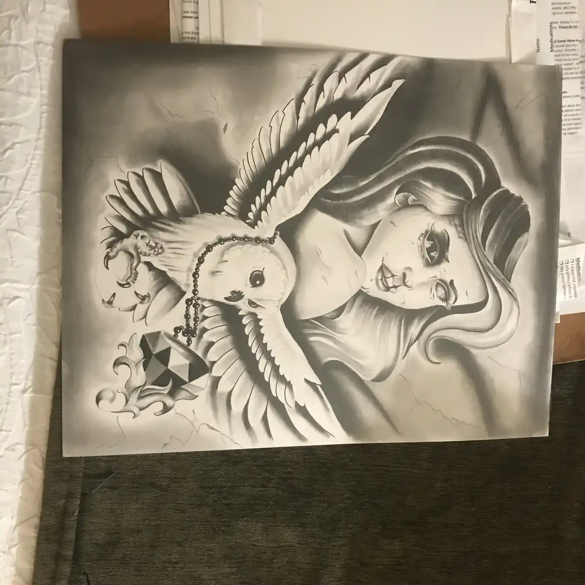 A black-and-white airbrush painting depicts a stylized, cartoonish owl with large eyes and a beak, wearing a beaded…