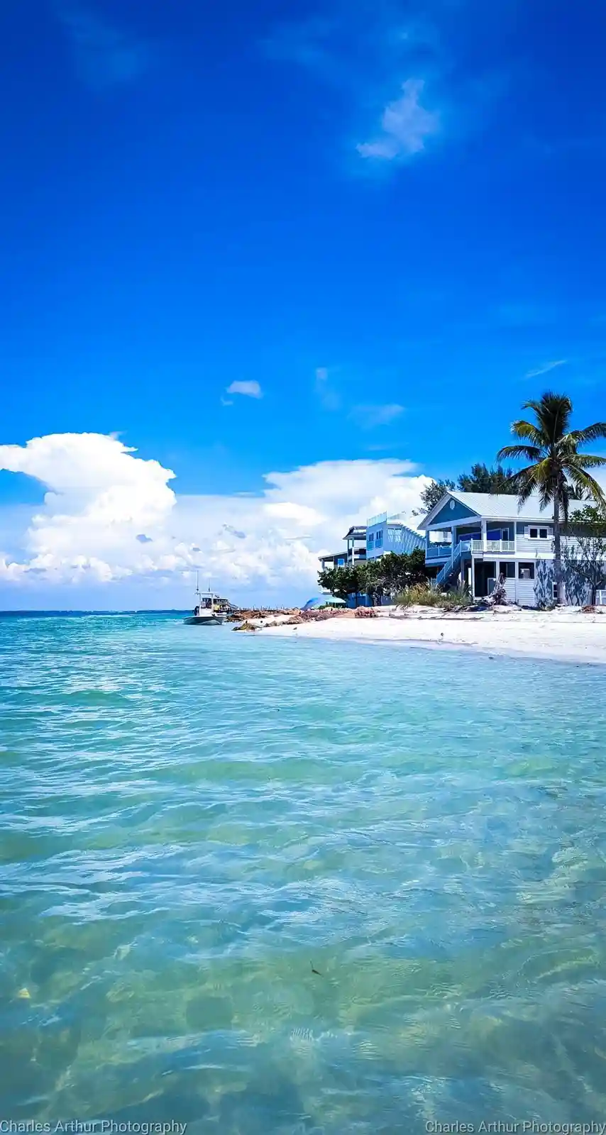 A vibrant tropical beach scene with clear turquoise water, white sand, and blue sky with fluffy clouds. On the shore, there…
