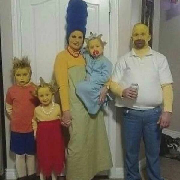 A family of five dressed as The Simpsons characters, with the mother in a tall blue beehive wig and yellow dress holding a…