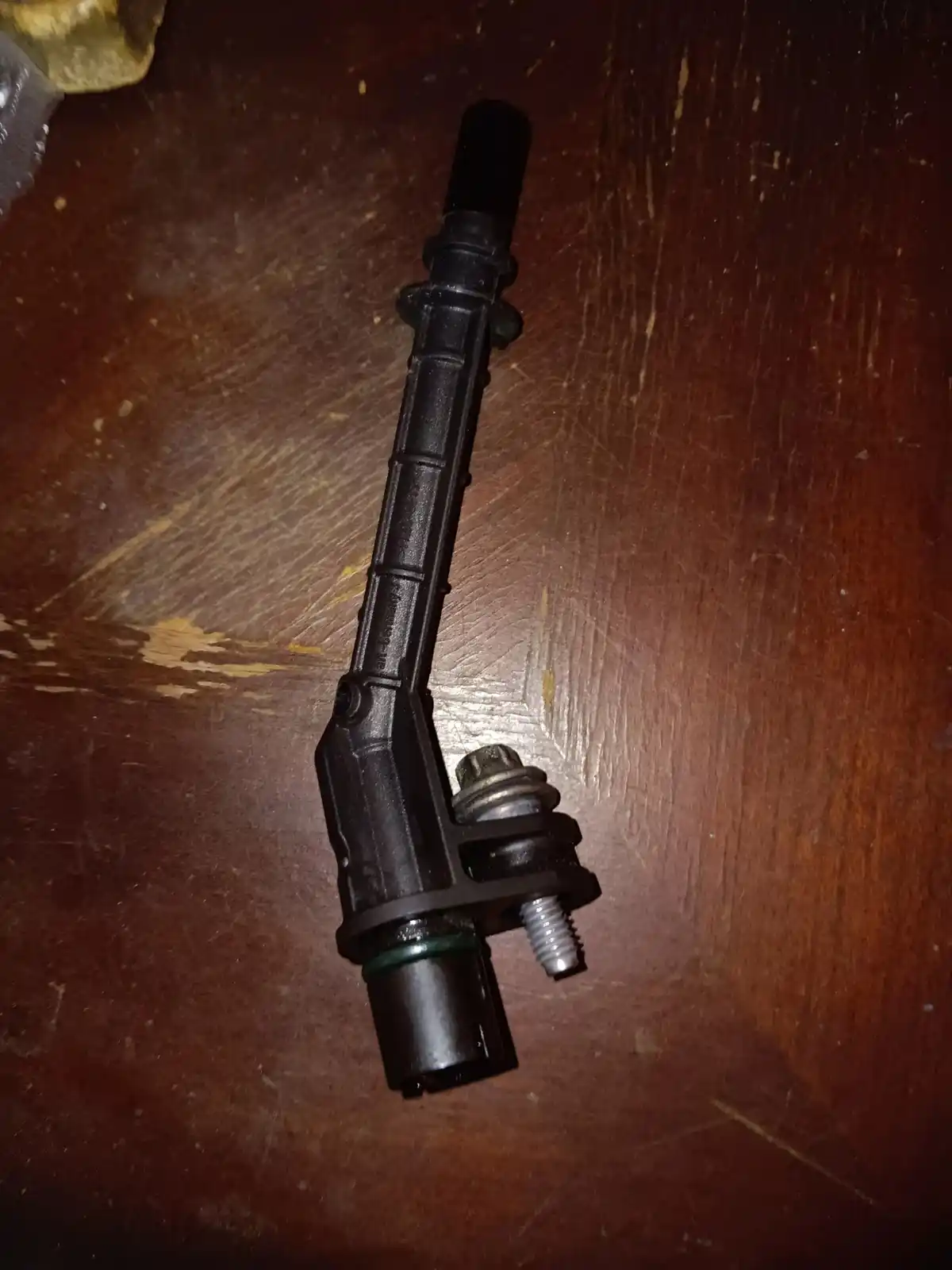 A close-up photo shows a black automotive throttle position sensor resting on a scratched wooden surface. The sensor has a…