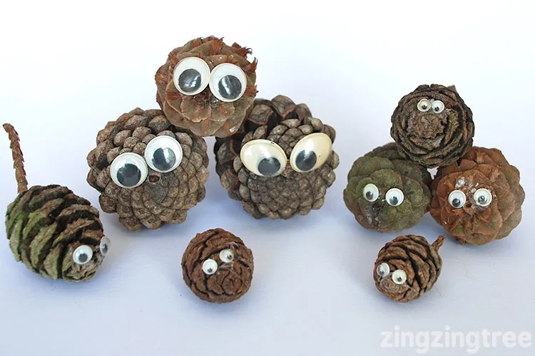 Several pinecones of various sizes are arranged on a white surface, each adorned with googly eyes to create a whimsical…
