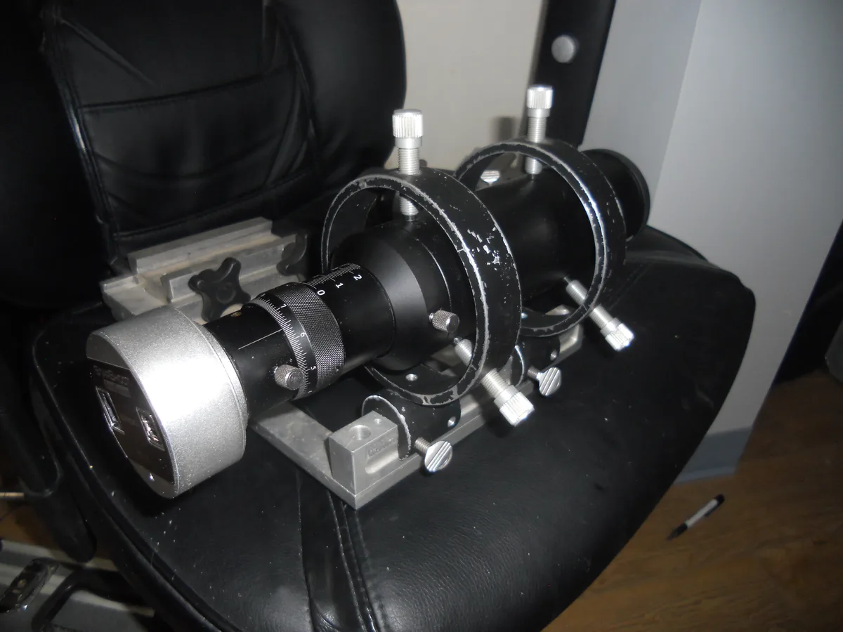 A complex, custom-built mechanical device with multiple adjustment knobs and rings sits on a black office chair. The device…