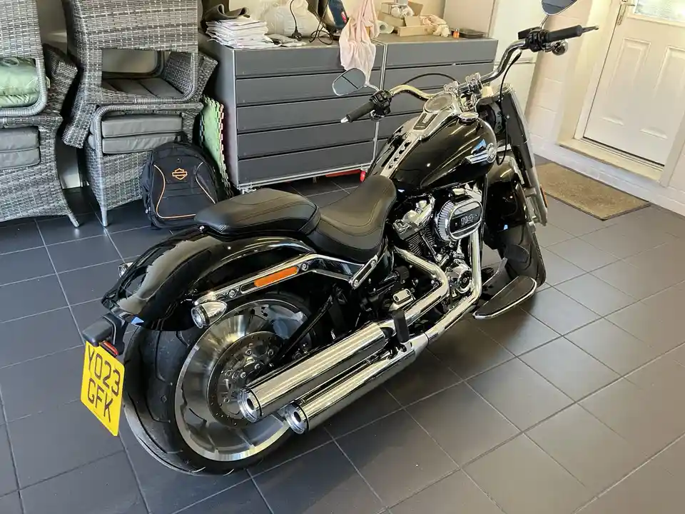 A black Harley-Davidson motorcycle with chrome accents is parked indoors on grey tiled flooring, next to wicker furniture…