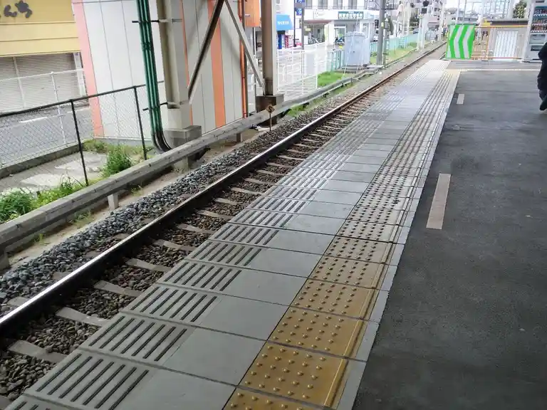 A photo of an empty train station platform with tracks running alongside, featuring tactile paving for the visually…