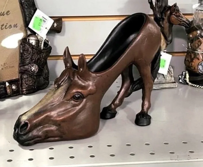 A bronze-colored decorative statue shaped like a high-heeled shoe, with the head and front legs of a horse forming the…
