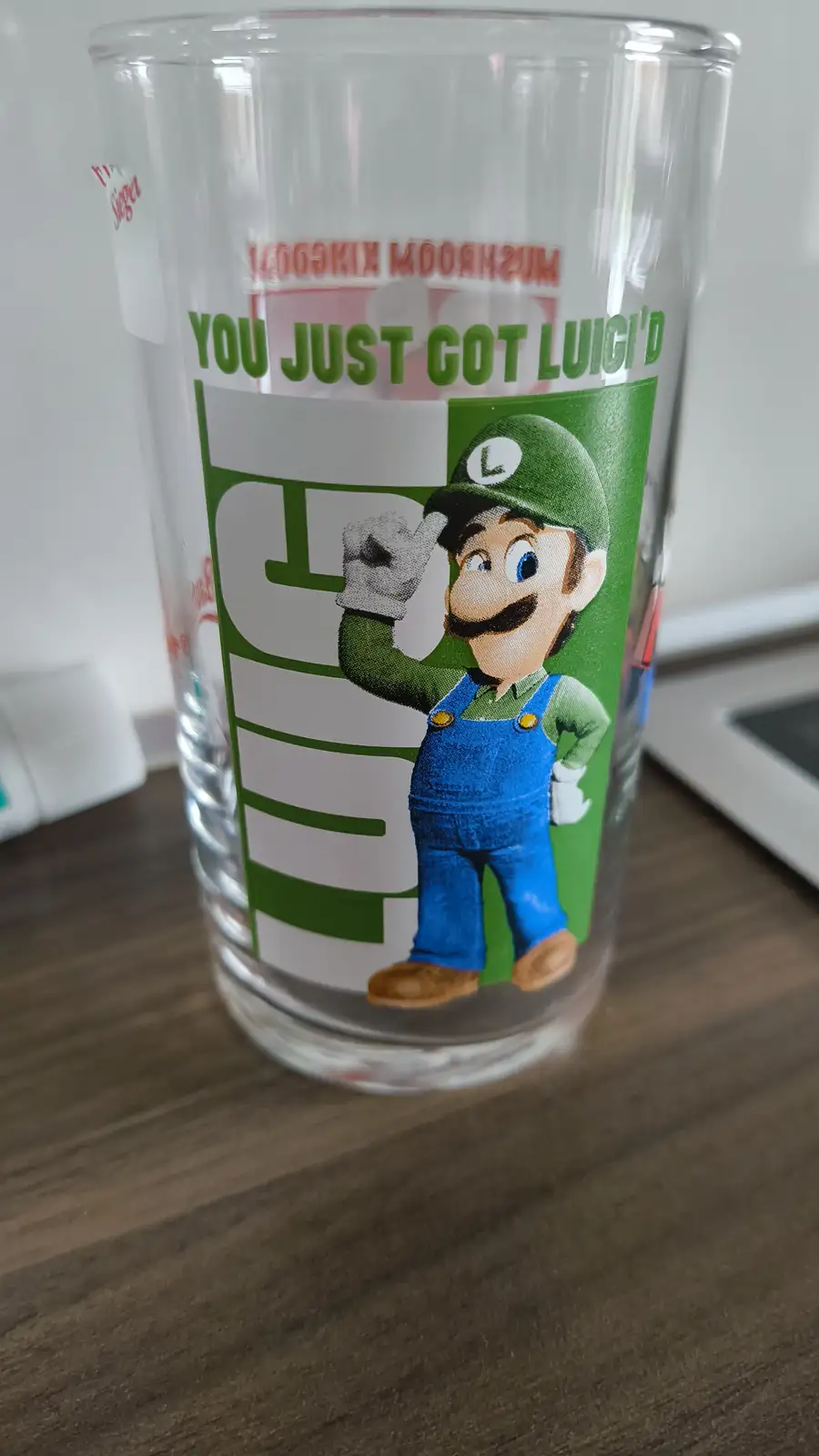 A clear glass tumbler with a printed design featuring the video game character Luigi from Super Mario, who is waving. The…