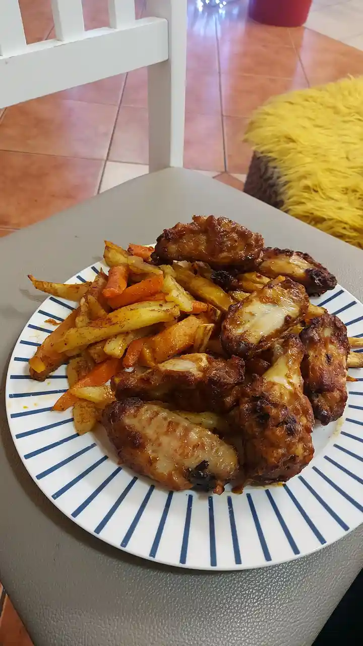 A plate of fried chicken wings and french fries sits on a gray chair, with a white chair and yellow fluffy object in the…