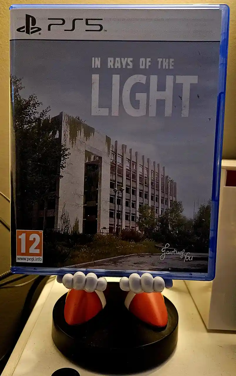 A PS5 game case for 'In Rays of the Light' featuring a desolate, overgrown building is humorously held up by a pair of…