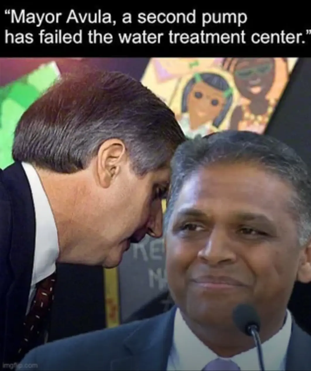 A man in a suit leans in to whisper into the ear of another man in a suit who is smiling calmly at a microphone. The text…