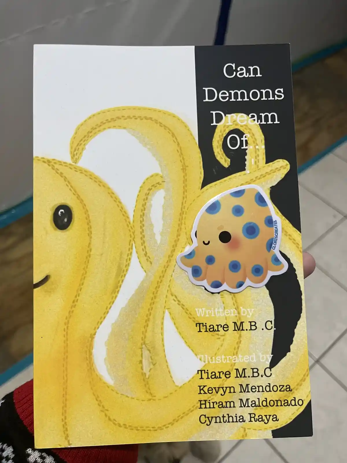 A book cover titled 'Can Demons Dream Of...' features a large, yellow, cartoonish banana with a smiling face and stitched…