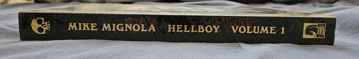 A close-up shot of the spine of a black comic book box set titled 'MIKE MIGNOLA HELLBOY VOLUME 1' in gold lettering, resting…