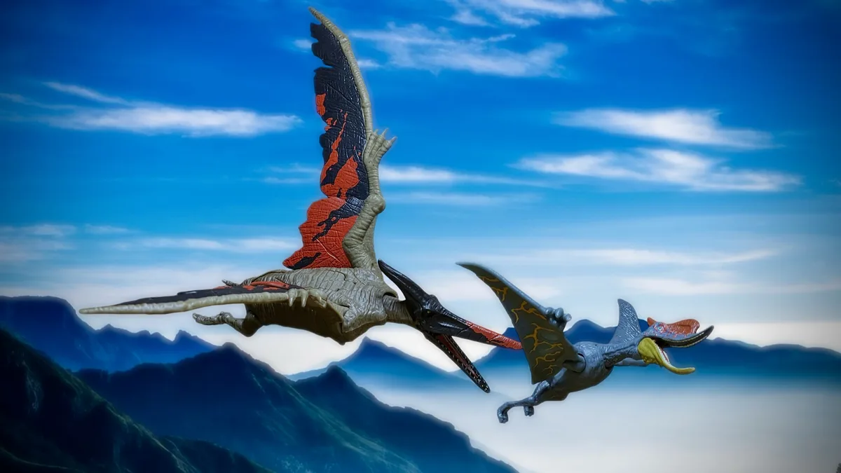 Two plastic pterosaur toys are shown flying against a backdrop of mountains and blue sky. The larger, greyish pterosaur on…