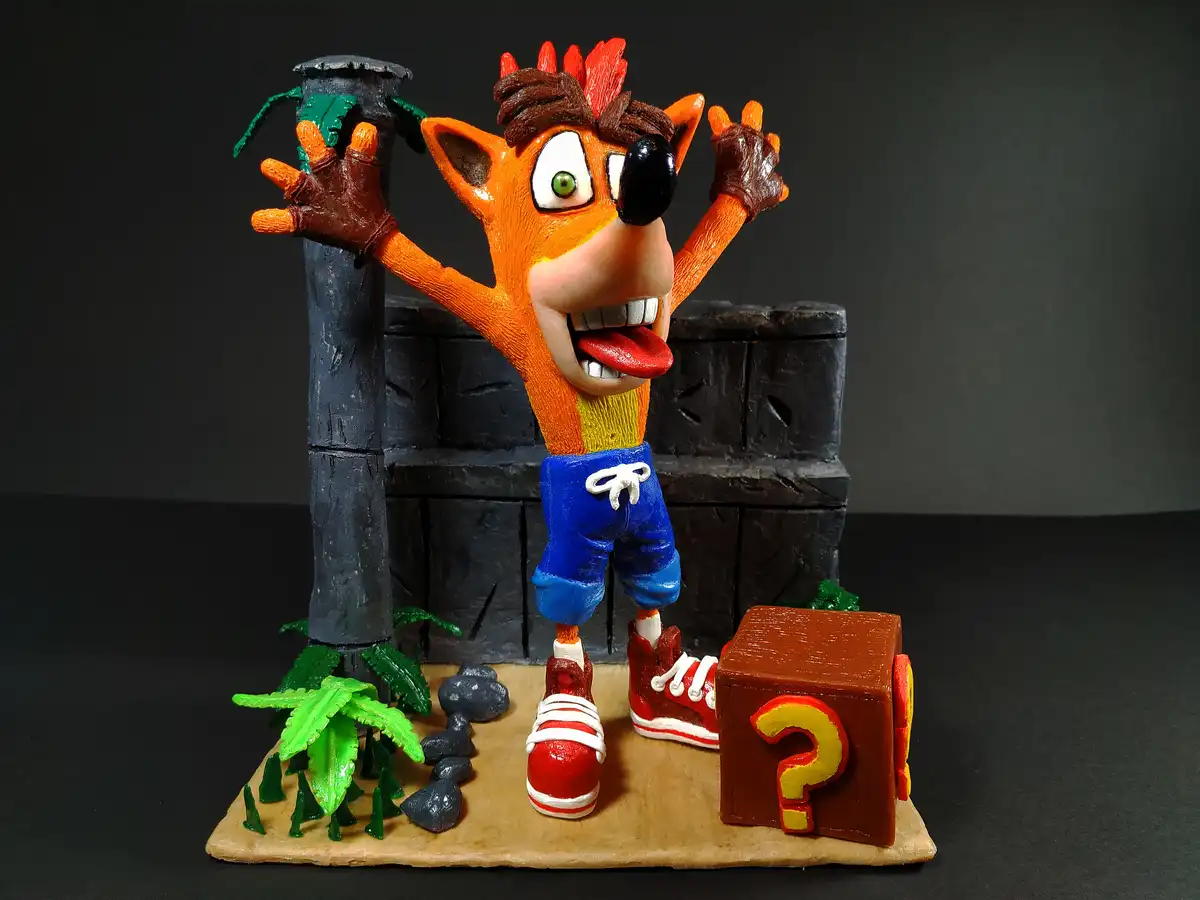 A figurine of the video game character Crash Bandicoot stands with arms raised in a startled pose, one eye covered by a…