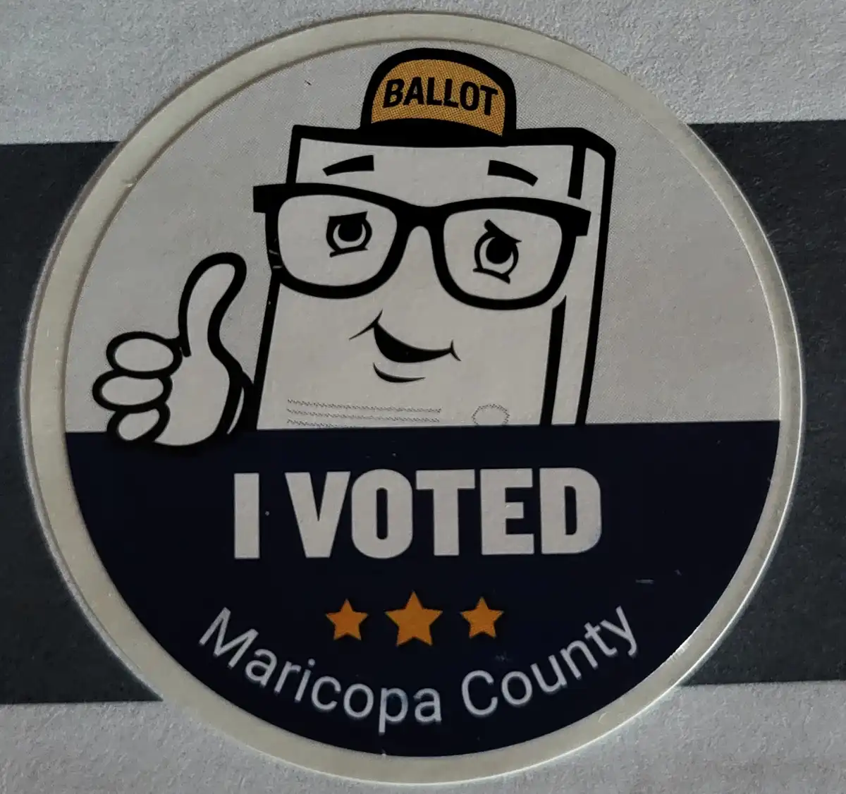 A circular 'I VOTED' sticker from Maricopa County features a cartoon ballot box with glasses and a 'BALLOT' cap, giving a…