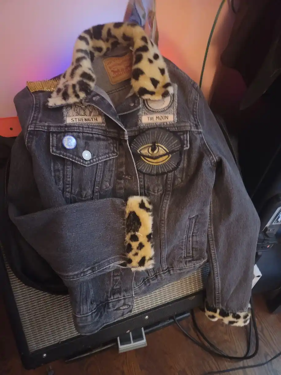A dark-wash denim jacket with leopard-print faux fur trim on the collar, cuffs, and sleeve ends, displayed on a…