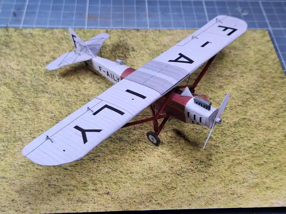A model of a vintage biplane with red and white paint sits on a grassy surface, its wings displaying the letters 'F-A-I-L-Y'…