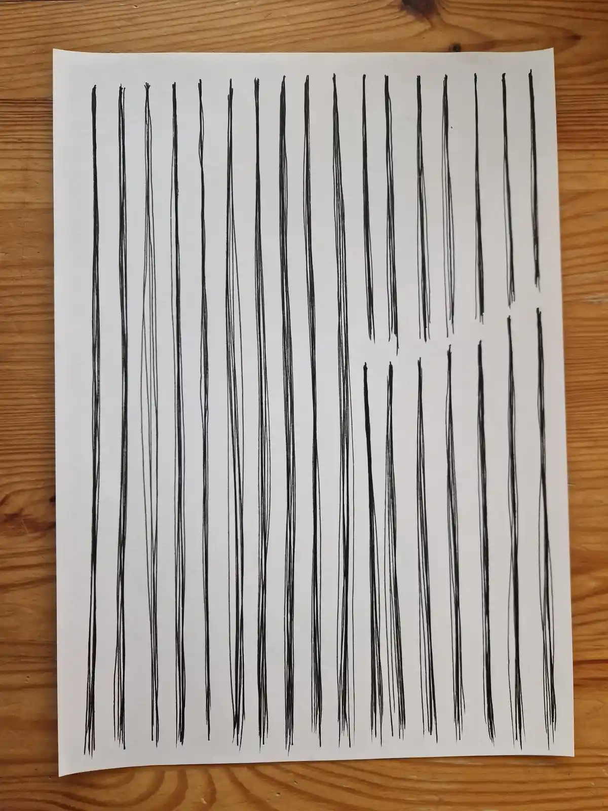 A white sheet of paper with numerous vertical black ink lines, some grouped and others spaced apart, rests on a wooden…