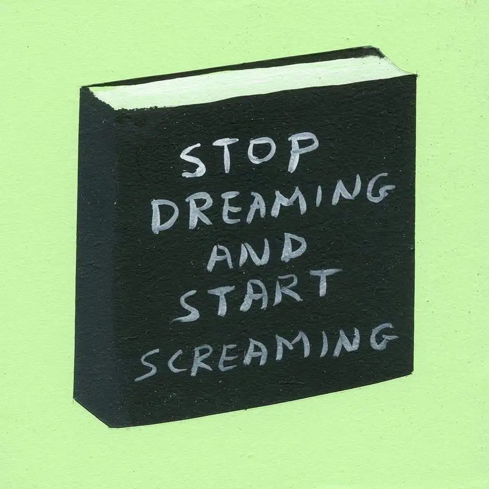 A hand-painted black book with white handwritten text that reads 'STOP DREAMING AND START SCREAMING' is centered against a…