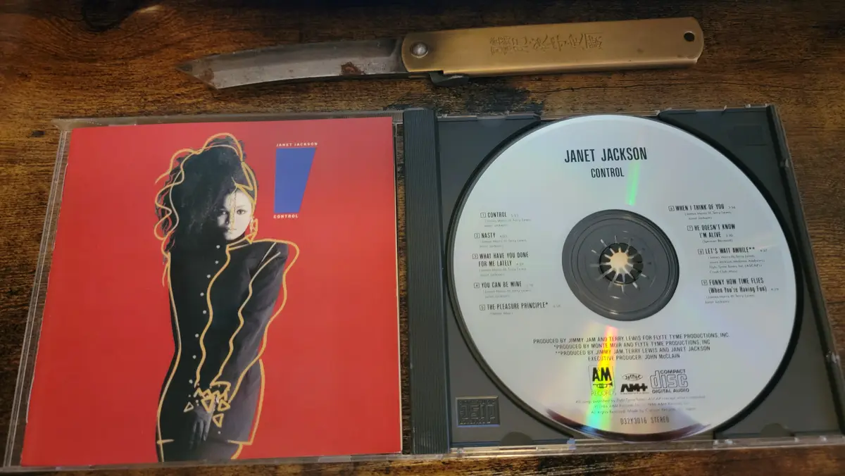 An open CD case for Janet Jackson's 1986 album 'Control' sits on a wooden surface, with the red cover art visible and the…