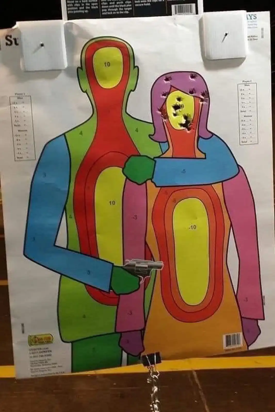 A colorful paper target depicting a man and a woman in a hugging pose, with the man holding a small revolver. The woman's…