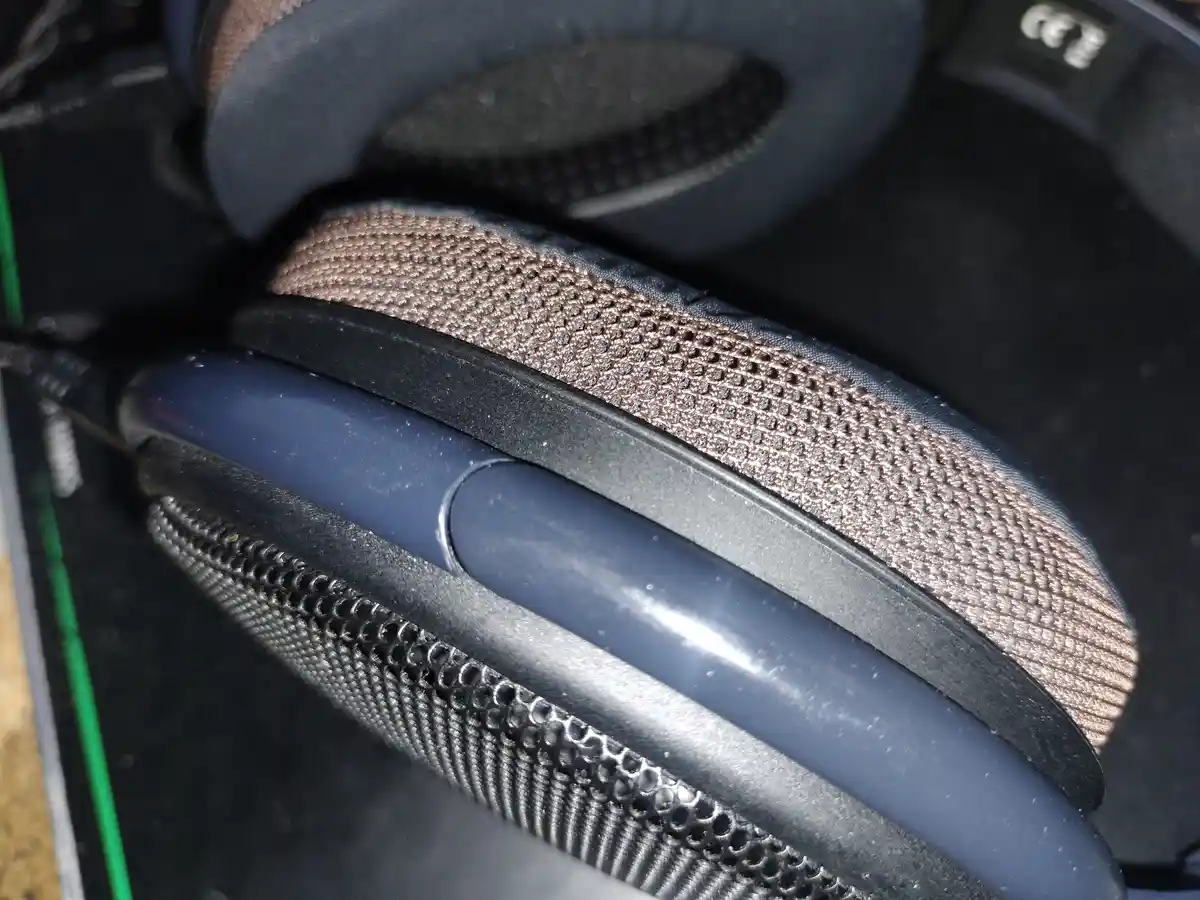 A close-up photo of a pair of over-ear headphones, showing the earcup padding, headband, and mesh grille. The overlaid text…