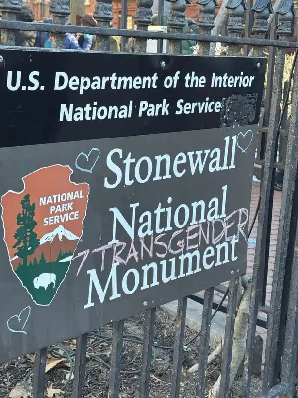 A black National Park Service sign for Stonewall National Monument, with 'TRANSGENDER' spray-painted over 'National' in pink…