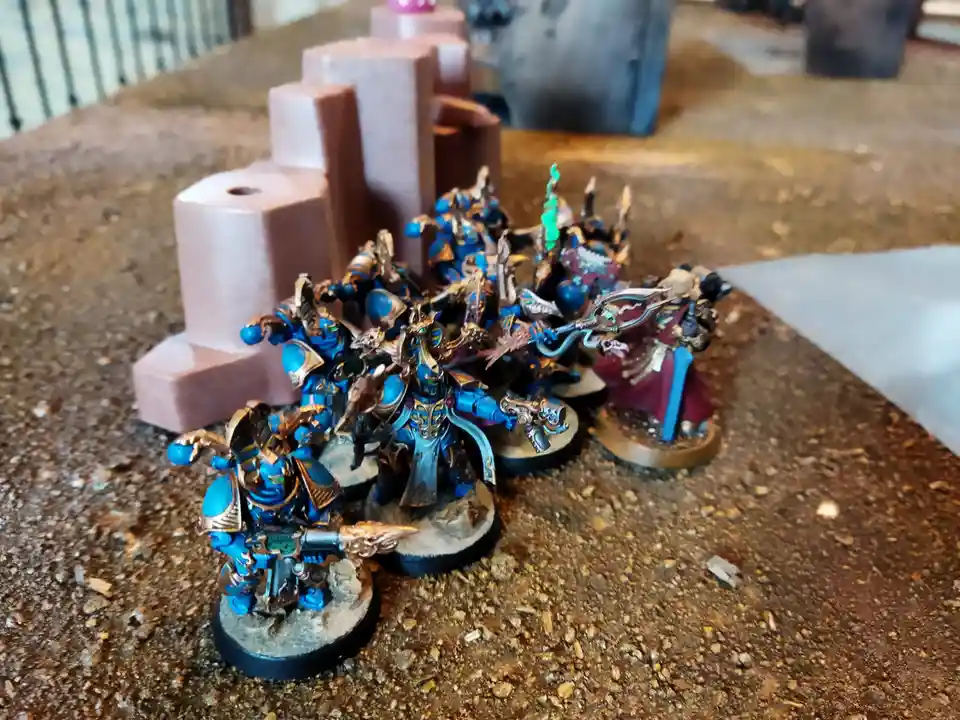 A photo of a collection of intricately painted blue and gold fantasy miniatures, likely from Warhammer 40,000, arranged on a…