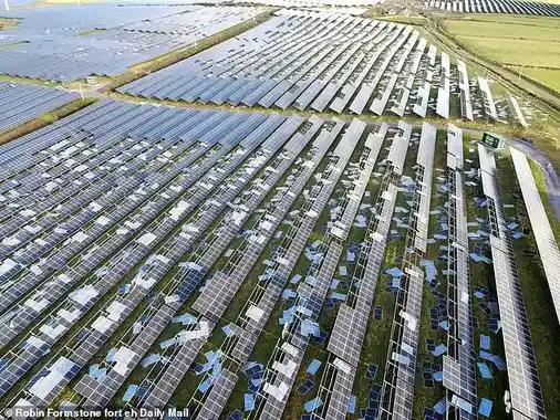 An aerial view shows a large field of solar panels, many of which are visibly broken or damaged, with blue and white…