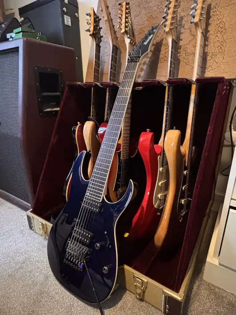 A blue electric guitar stands upright in front of several other guitars stored vertically in open, burgundy-lined cases…