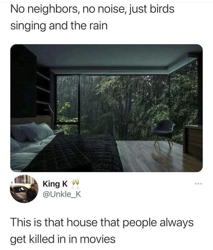 A serene bedroom with a large glass wall overlooking a rainy forest, featuring a bed, a chair, and dark wood flooring. The…