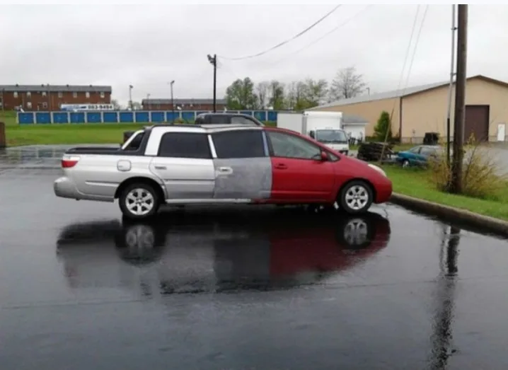 A pickup truck is parked on a wet street, its body painted half silver and half red, creating a stark visual split down the…